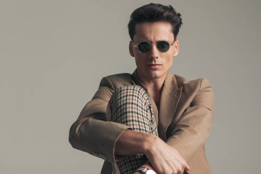 sexy young man with dark hair holding knee up and posing in a cool way on grey background in studio