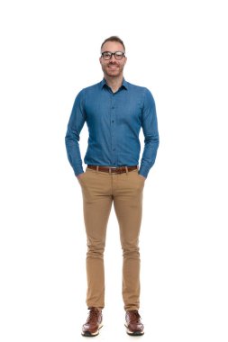 full body picture of handsome casual man with glasses posing with hands in pockets and smiling on white background in studio