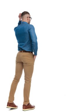 confused young man in denim shirt scratching head and thinking of ways to solve difficult problems while walking with hand in pocket on white background
