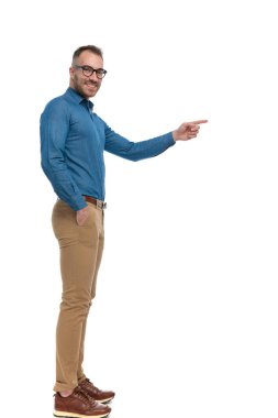 side view of handsome guy standing in line with hand in pocket and pointing finger while smiling on white background in studio
