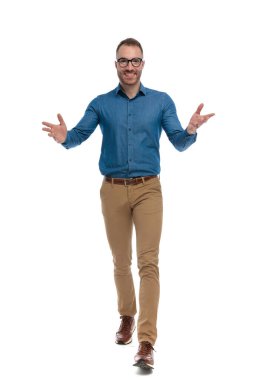 happy nerdy man with glasses opening arms and gesturing while walking on white background in studio