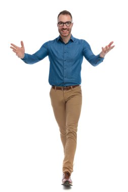 excited casual man with glasses opening arms and walking while smiling on white background in studio