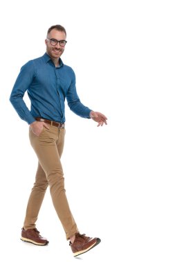 attractive young guy with glasses smiling and walking with hand in pocket on white background in studio