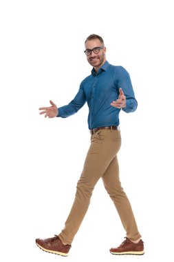full body picture of handsome nerdy man with glasses walking, smiling and gesturing on white background in studio