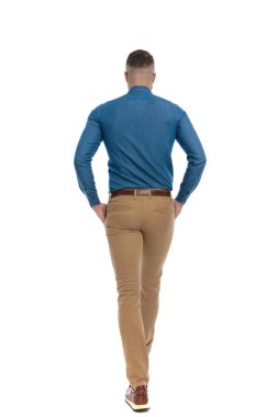 behind view picture of sexy man stepping with hands in pockets in front of white background in studio