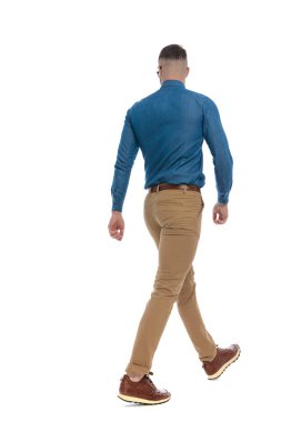 back view picture of casual young guy in denim shirt walking in front of white background in studio