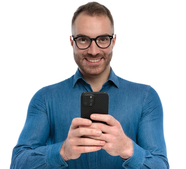 幸せな髭を生やした男が携帯を持ちソーシャルメディアをスクロールして笑顔でスタジオで白い背景にポーズをとって — ストック写真