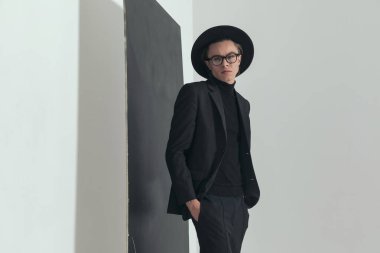 portrait of handsome young guy holding hands in pockets and posing in front of black board on grey background in studio
