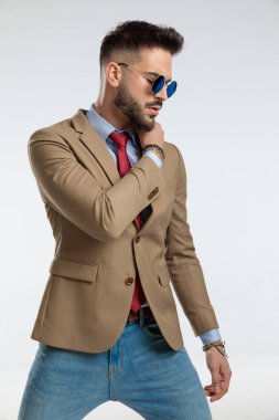 portrait of a attractive businessman posing with macho vibe, standing, wearing sunglasses against gray studio background