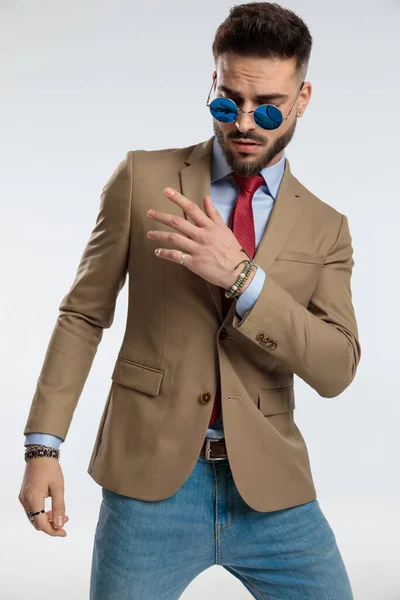 portrait of a attractive businessman with a dramatic pose, standing, wearing sunglasses against gray studio background