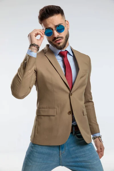 portrait of a young businessman with cool style, standing, arranging sunglasses against gray studio background