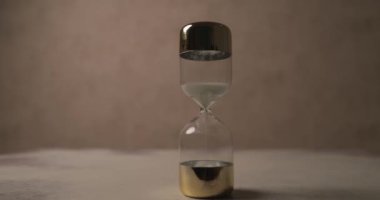 project video of hourglass as a time pressure illustrating the concept of time ticking away in front of brown background