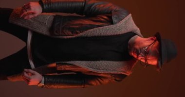 fashion casual guy looking down, arranging leather jacket and hat and walking away while colorful lights on background