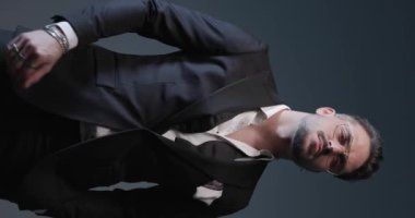 project video of sexy young best man in spotlight wearing tuxedo, adjusting ring, rubbing palms, looking to side and snapping fingers