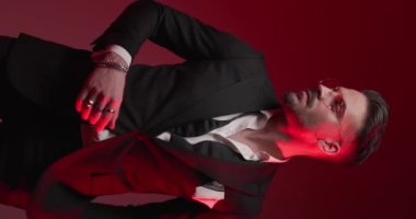 vertical video with police lights on of elegant young best man adjusting tuxedo, rings and glasses and looking to side while rubbing palms