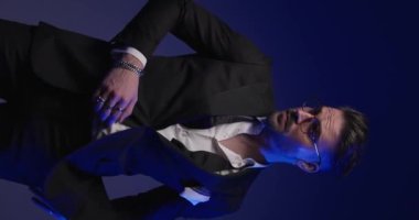 elegant young groom with hand in pockets looking to side, buttoning tuxedo, looking to side and rubbing palms with police lights on