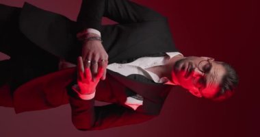 vertical video with police lights on of elegant man rubbing palms, looking to side, holding hands in pockets, smiling and arranging glasses