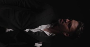 vertical video with lightning of elegant young groom looking to side, adjusting eyeglasses and looking down