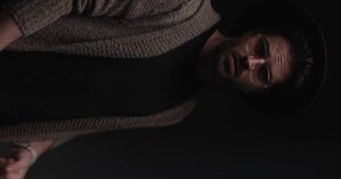 vertical video with flash of sexy casual guy arranging hat, looking down and crossing arms while confidently posing and looking to side
