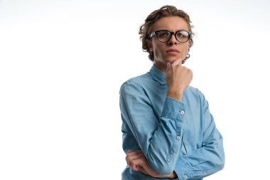 Portrait of attractive casual man thinking hard about something, standing, wearing eyeglasses against white studio background