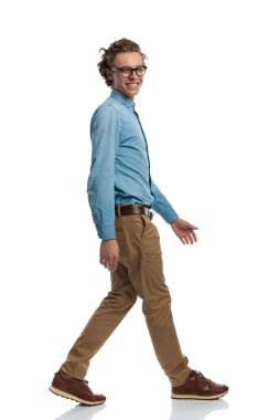 Full body picture of young casual man walking and looking over his shoulder, standing, wearing eyeglasses against white studio background