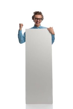 Full body picture of handsome casual man presenting billboard while celebrating success, standing, wearing eyeglasses against white studio background