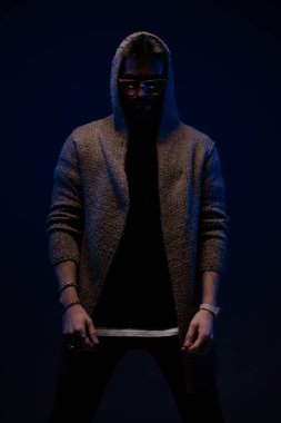 dramatic cool guy with sunglasses wearing wool cardigan and posing on dark background