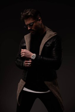 cool young guy with glasses arranging sleves and looking down while posing on grey background