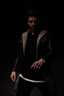 mysterious young man wearing hat and sunglasses and posing on grey background 