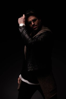 sexy young man with glasses looking away and adjusting hat in front of grey background