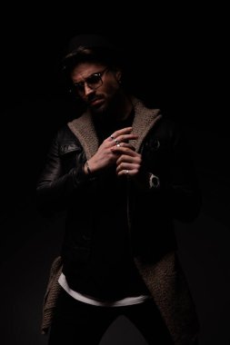 mysterious bearded man with hand and glasses adjusting rings on fingers and posing on a grey background