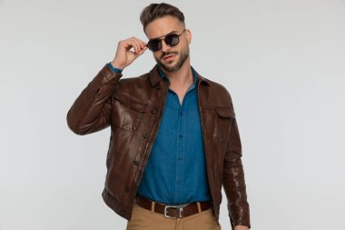 portrait of a attractive casual man arranging his cool sunglasses, standing, against gray studio background