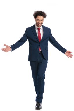 handsome young businessman with curly hair opening arms and welcoming, walking in front of white background in studio