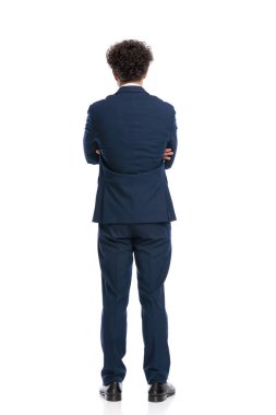 rear view of elegant young businessman in suit crossing arms and standing in front of white background in studio