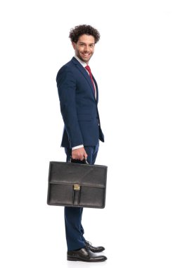 side view of happy elegant businessman holding suitcase and smiling in front of white background in studio