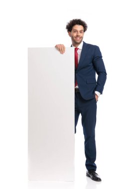confident elegant man in suit presenting white empty billboard and smiling on white background