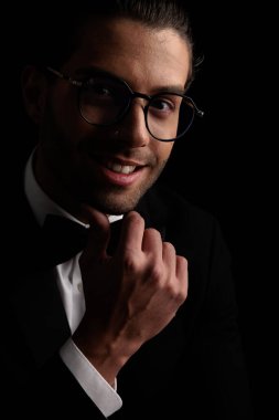 happy arabic groom with glasses touching chin, smiling and thinking about his dream life on black background