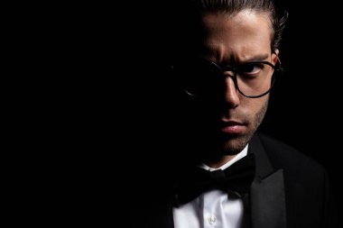 close up portrait of handsome turkish man with glassess wearing tuxedo and posing in a mysterious way with light on black background