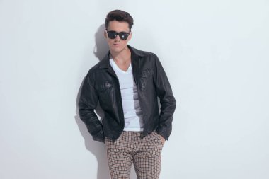 Portrait of  handsome casual man with macho vibe posing, standing, wearing sunglasses in a fashion pose