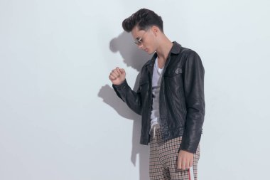 Portrait of  young casual man posing while looking down with dramatic stance, standing, wearing sunglasses in a fashion pose