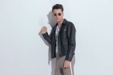 Portrait of  attractive casual man posing with cool style, standing, wearing sunglasses in a fashion pose