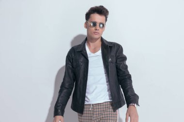 Portrait of  attractive casual man with cool vibe posing, standing, wearing sunglasses in a fashion pose