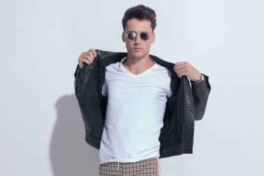 Portrait of  handsome casual man arranging his jacket on his body, standing, wearing sunglasses in a fashion pose