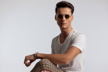Portrait of young casual man posing with cool sunglasses, sitting, wearing sunglasses in a fashion pose