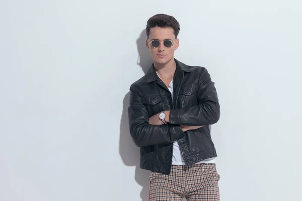 Portrait of  attractive casual man rocking a cool leather jacket, standing, wearing sunglasses in a fashion pose