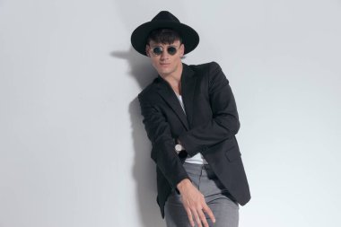 Portrait of young smart casual man crossing his hands and smiling, standing, wearing a black hat and sunglasses in a fashion pose