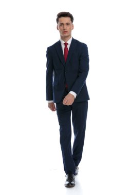 young businessman walking and looking at the camera, wearing a suit and tie against white background