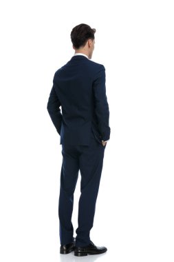 attractive businessman looking away with hands in pockets, wearing a suit and tie against white background