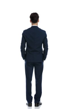 handsome businessman showing his back with hands in pockets, wearing a suit and tie against white background