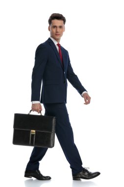 handsome businessman walking and holding a briefcase to the side, wearing a suit and tie against white background